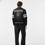 Black Cowboys varsity jacket with star logo, striped sleeves, and back text, worn by model in studio
