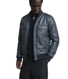 Men's dark gray leather bomber jacket with front pockets and ribbed cuffs, styled over a navy sweater