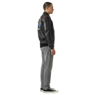 Men's black leather bomber jacket with patch, paired with gray jeans and sneakers