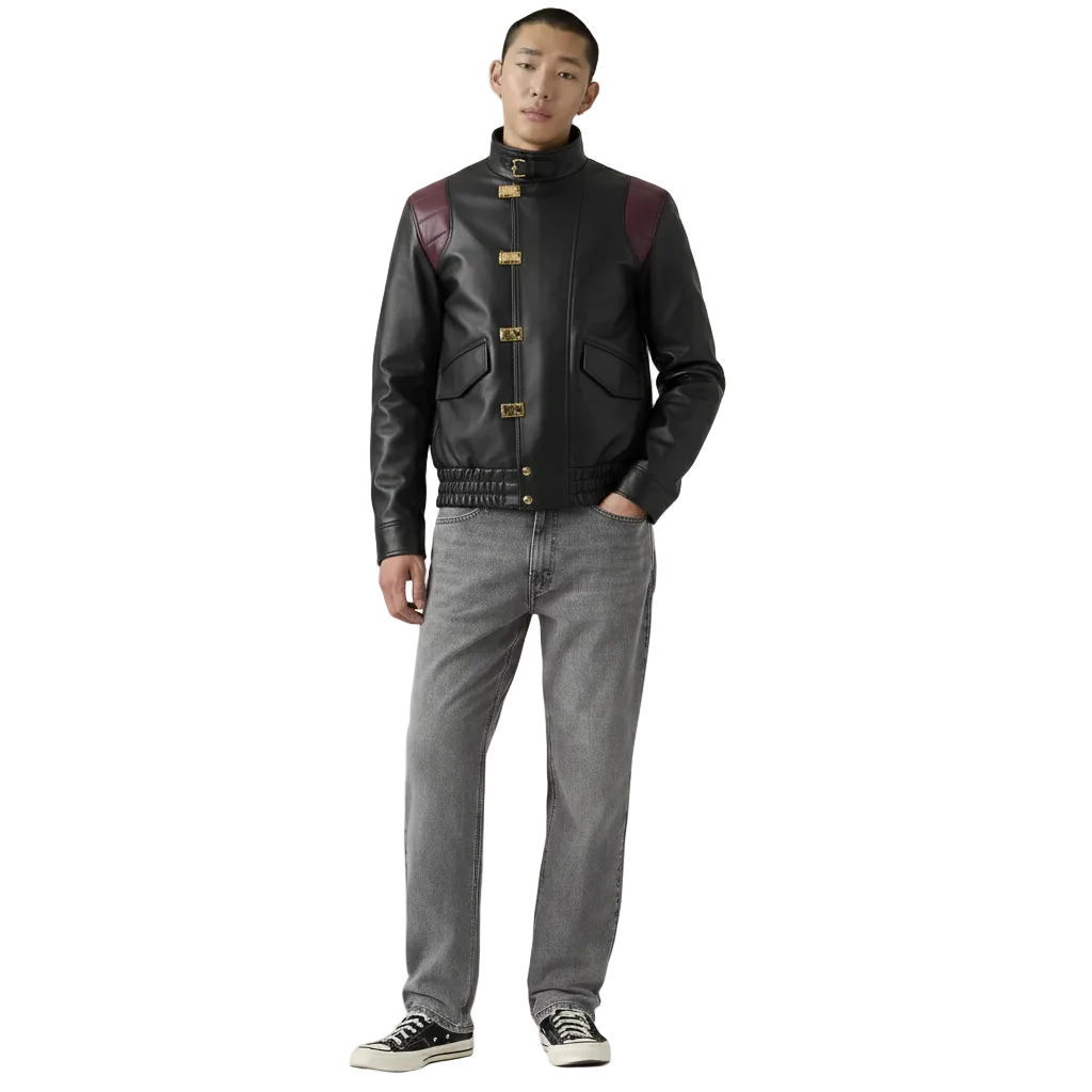 Men's black leather jacket with burgundy shoulder panels and gold hardware, styled with gray jeans and sneakers