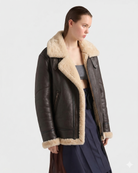 Women's brown leather shearling coat with cozy cream lining, styled with gray top and navy skirt.