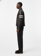Man in black leather moto jacket with white stripes, paired with dark jeans and casual shoes