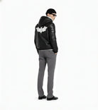 Men's black leather jacket with white bat emblem, styled with gray pants and beanie