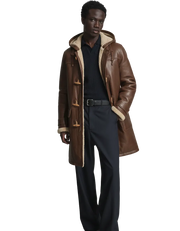 Men's brown shearling coat with hood, toggle closures, and wool lining, styled with navy pants and sweater