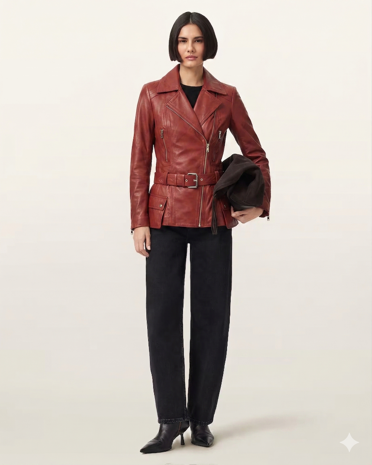 Woman in red leather moto jacket with belt, black jeans, and heels, holding hat