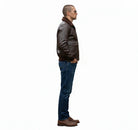 Man in brown leather bomber jacket with shearling collar, blue jeans, and brown shoes, side view