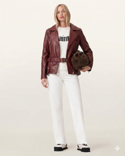 Woman in burgundy leather moto jacket, white jeans, and graphic sweater, holding brown bag