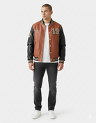 Men's brown and black varsity jacket with number 19, styled with white tee and dark jeans