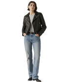 Woman wearing black leather jacket, gray tee, and blue jeans with hands in pockets
