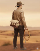 Man in desert wearing brown leather jacket, hat, and canvas satchel, holding coiled rope