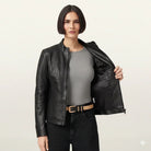 Woman modeling black leather jacket with zipper, gray top, and black jeans, showcasing inner lining.