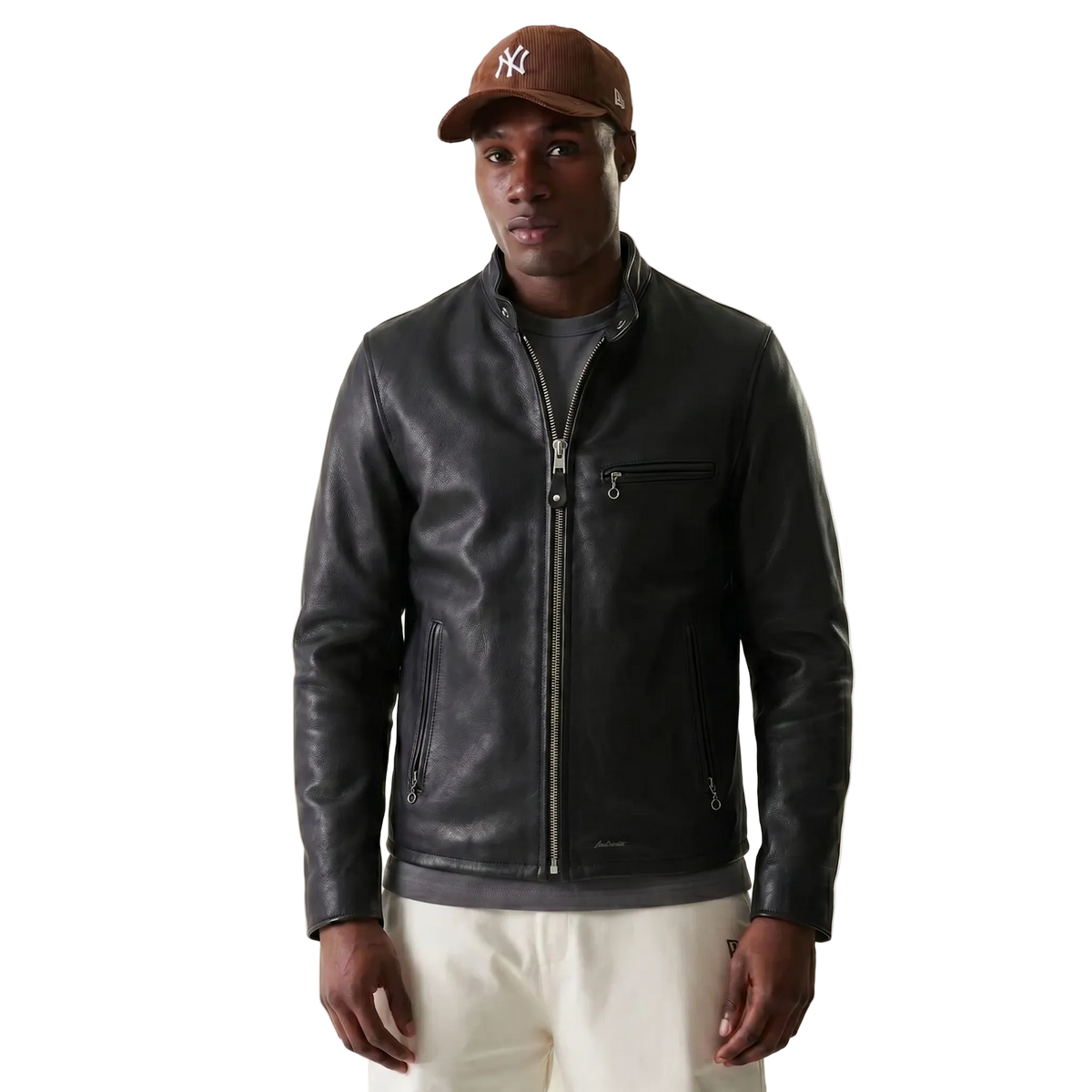 Men's black leather jacket with front zipper and side pockets, styled with cap and casual pants