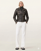 Woman in black quilted leather biker jacket with gold zippers, white pants, and chunky sneakers