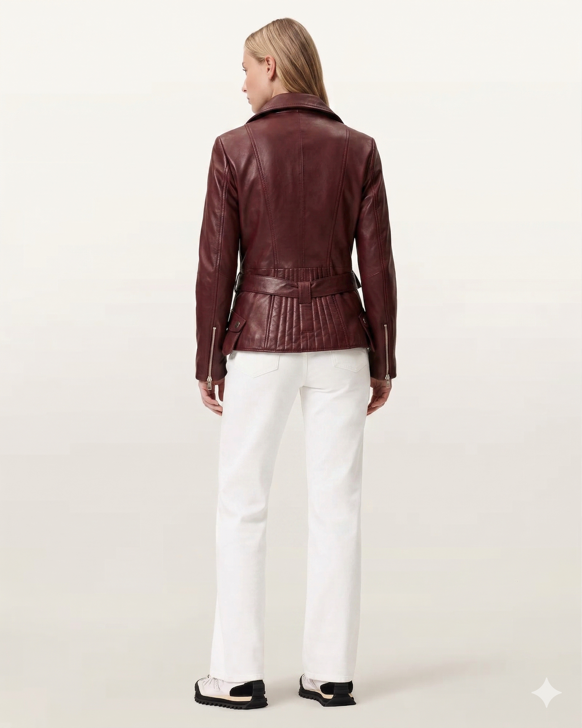 Woman wearing burgundy leather moto jacket with belt back view, paired with white pants