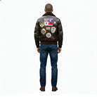 Men's brown leather bomber jacket with vintage aviation patches, worn with blue jeans