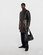 Men's black leather coat with tan trim, styled with matching bag and sunglasses for modern streetwear look