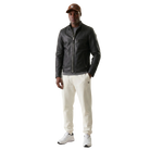 Men's black leather jacket with zipper, paired with cream joggers and white sneakers, styled with a brown cap.