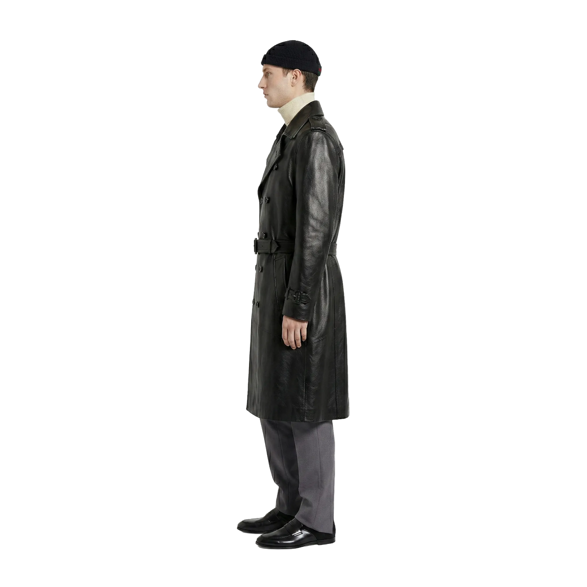 Man wearing black leather trench coat with belt, beanie, and gray trousers, side view