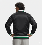 Black satin bomber jacket with green and white ribbed trim, worn by man with hands on hips