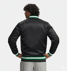 Black satin varsity jacket with green and white ribbed trim, worn by man with hands on hips